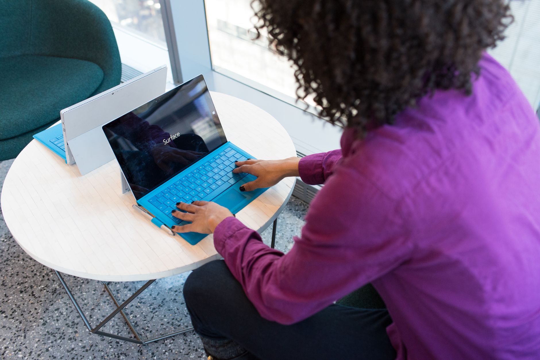 A woman typing on a laptop at a round table in a modern indoor setting. (Photo by Christina Morillo on Pexels)