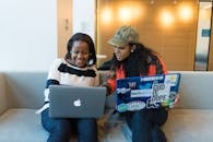 两名女性在室内一起工作，她们在笔记本电脑上配对编程，分享想法