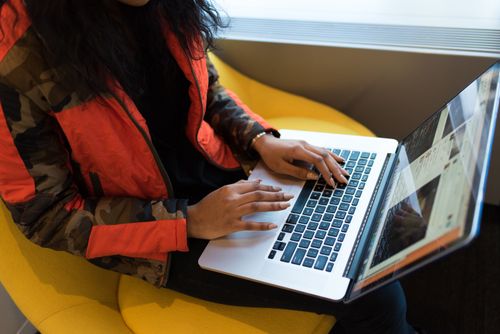 Free A woman typing on a laptop in an office, wearing a red jacket, showing focus and technology use. Stock Photo