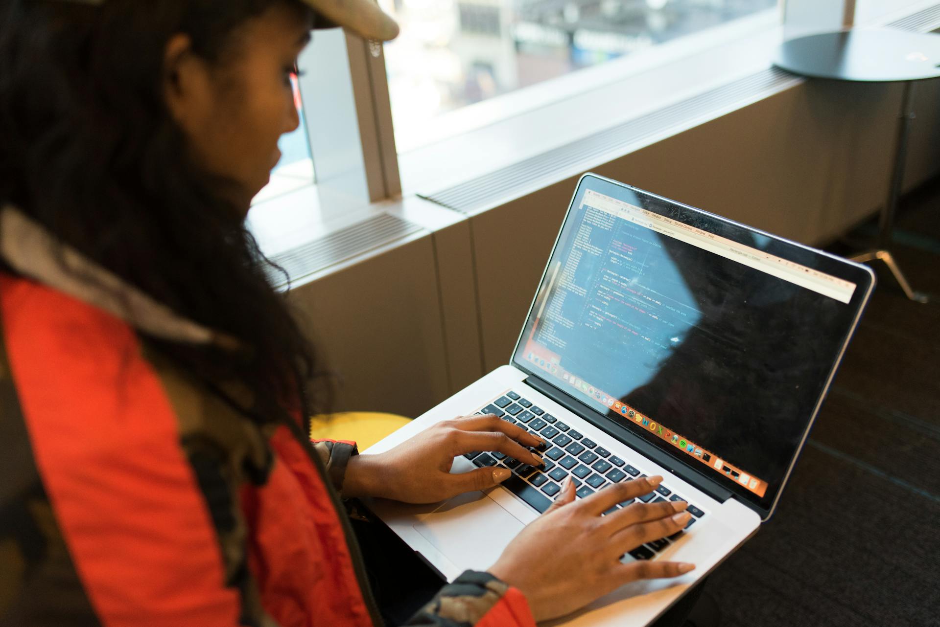 A focused woman typing code on her laptop indoors, embodying tech innovation.