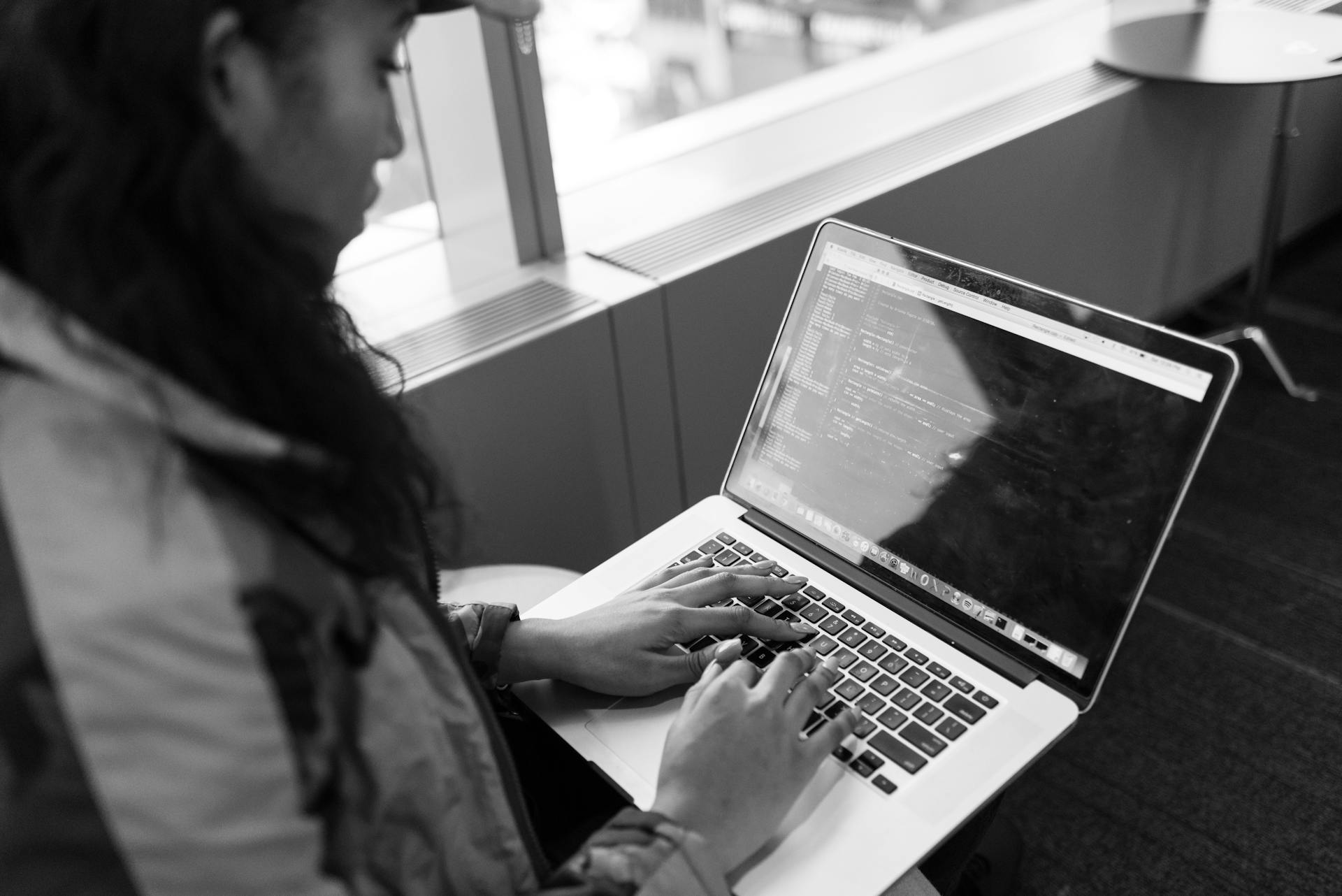 A woman typing code on a laptop in a modern indoor setting, showcasing tech work.