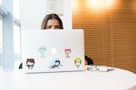 一名女子在现代室内环境中，正对着一台贴着科技主题贴纸的笔记本电脑工作