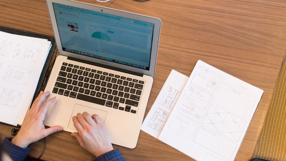 An overhead view of a person working on a laptop at a desk with documents and papers.