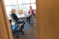 两名职业女性在现代办公室里用笔记本电脑和文件讨论工作