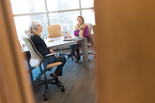 两名职业女性在现代办公室里用笔记本电脑和文件讨论工作