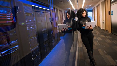 A woman using a laptop navigating a contemporary data center with mirrored servers.