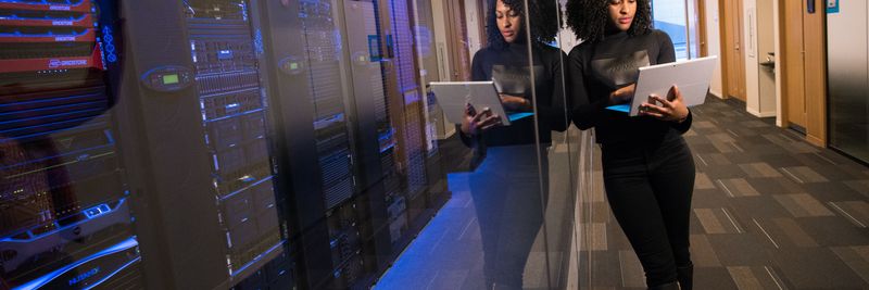 A woman using a laptop navigating a contemporary data center with mirrored servers.