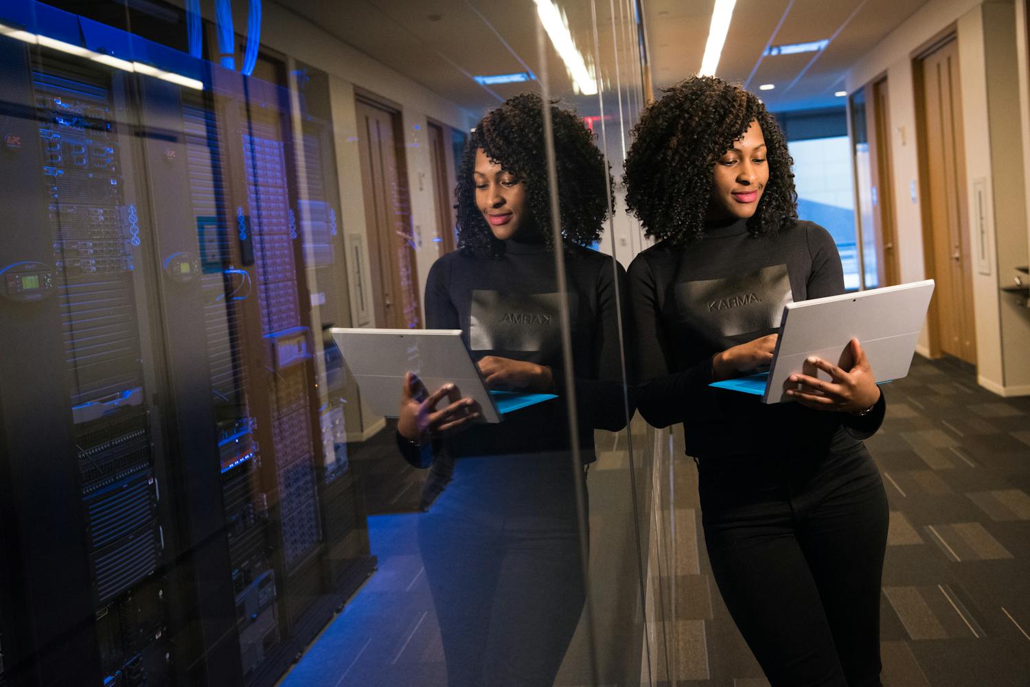 African American woman standing in modern office using laptop, reflecting professionalism and technology engagement