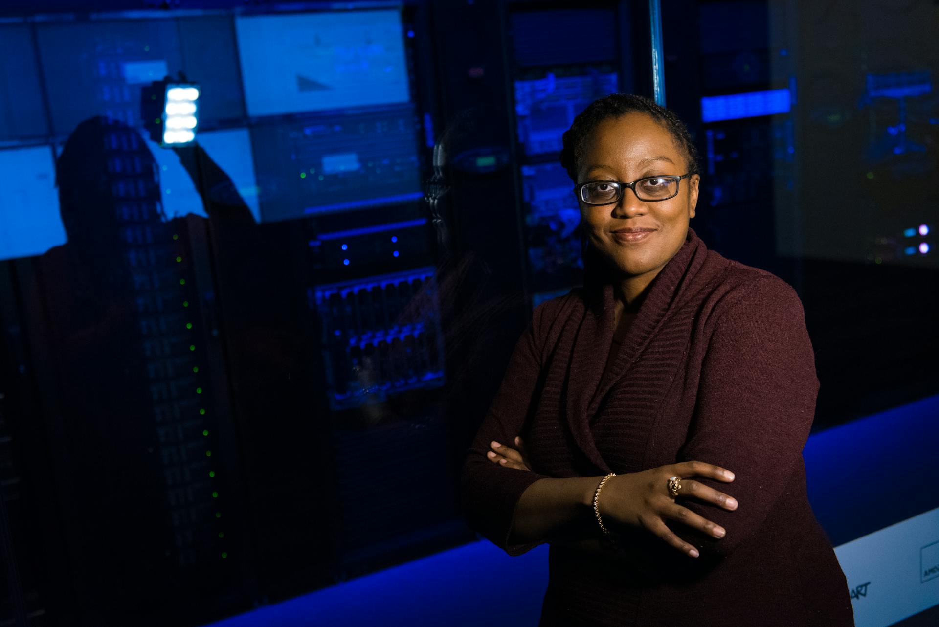 Professional woman standing confidently in a data center, surrounded by glowing servers.