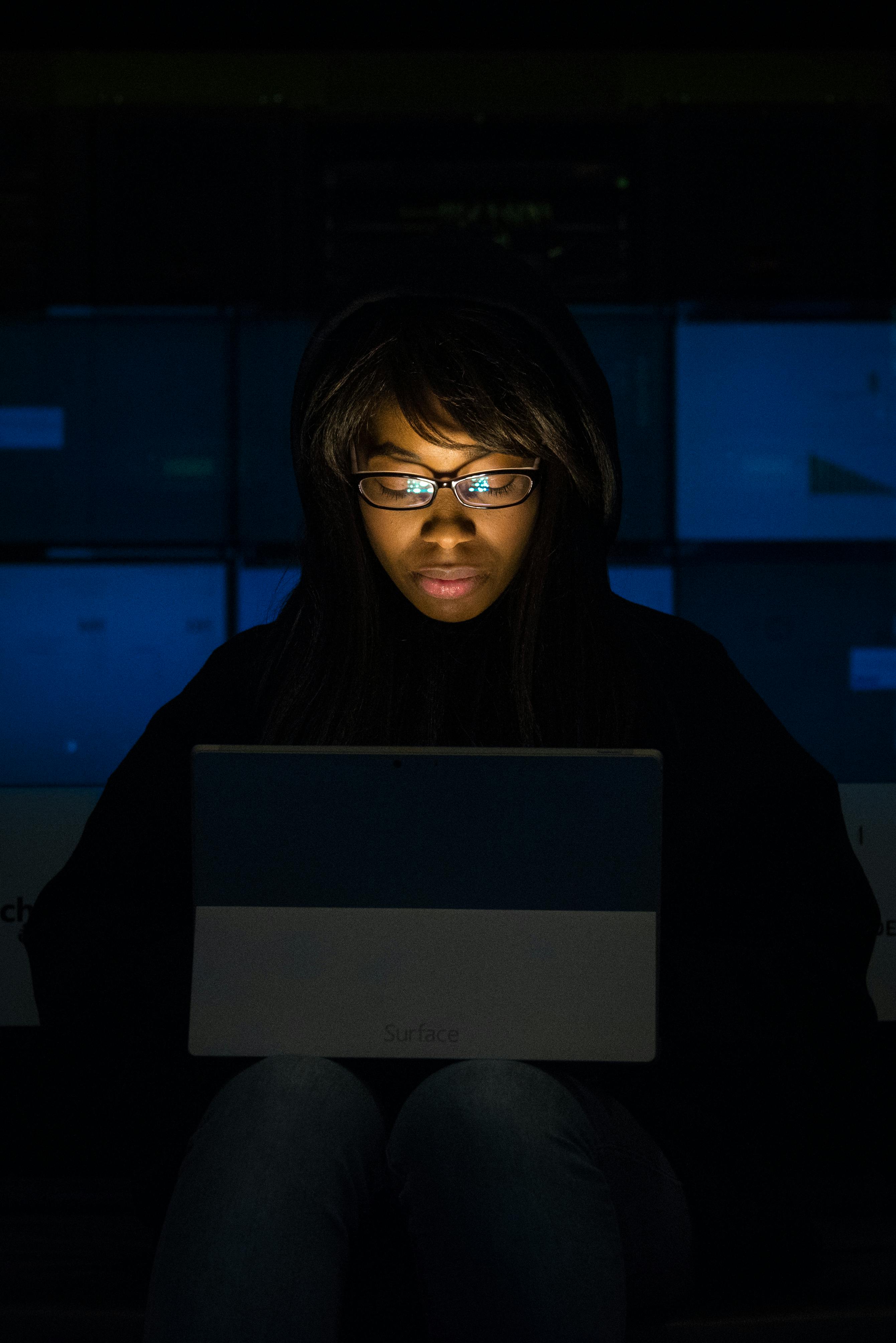 woman wearing eyeglasses looking at tablet computer in dark room