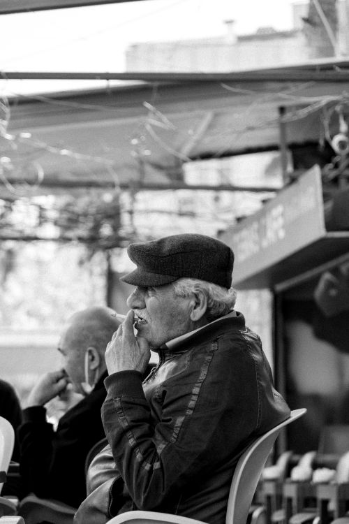 Free Black and white photo of an elderly man seated outdoors, enjoying a moment of relaxation at a café. Stock Photo