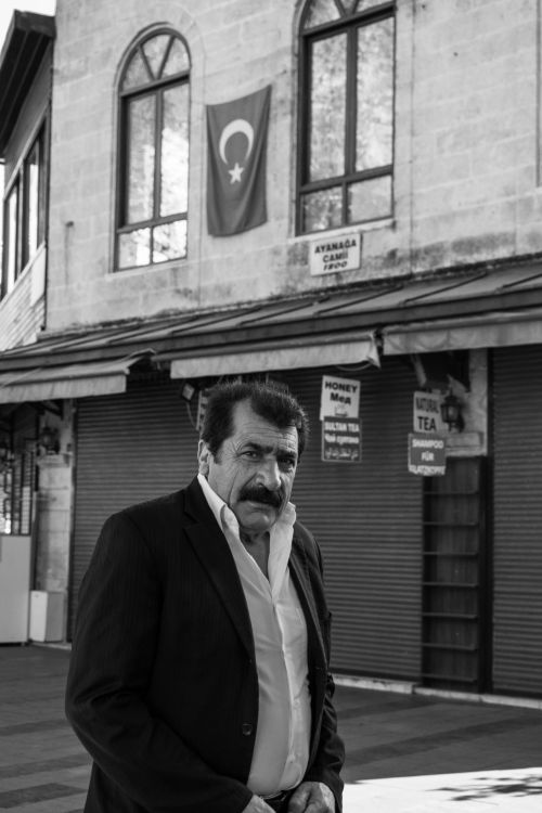 Free A monochrome portrait of a man standing on a Turkish street, featuring traditional architecture and the national flag. Stock Photo