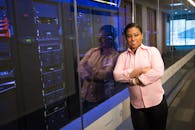 一位黑人女工程师自信地微笑着，交叉双臂站在服务器室里