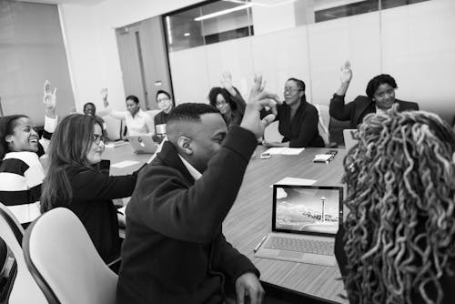 Grayscale Photo of Group of People Raises Hands