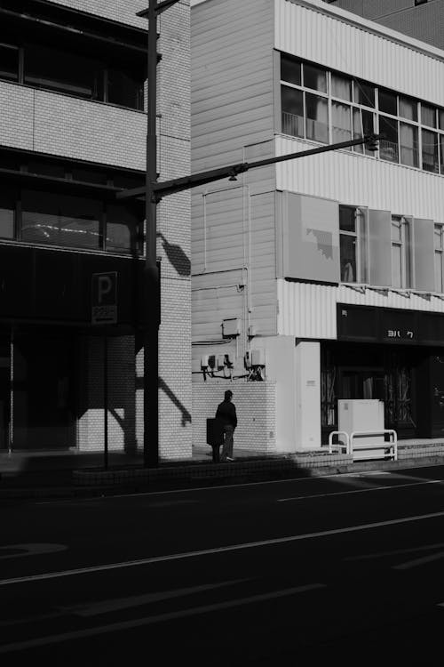 Grayscale Photo of Person Walking on Sidewalk Near Buildings