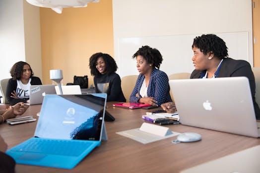 Black women collaborating with laptops in an office meeting, enhancing teamwork and technology.