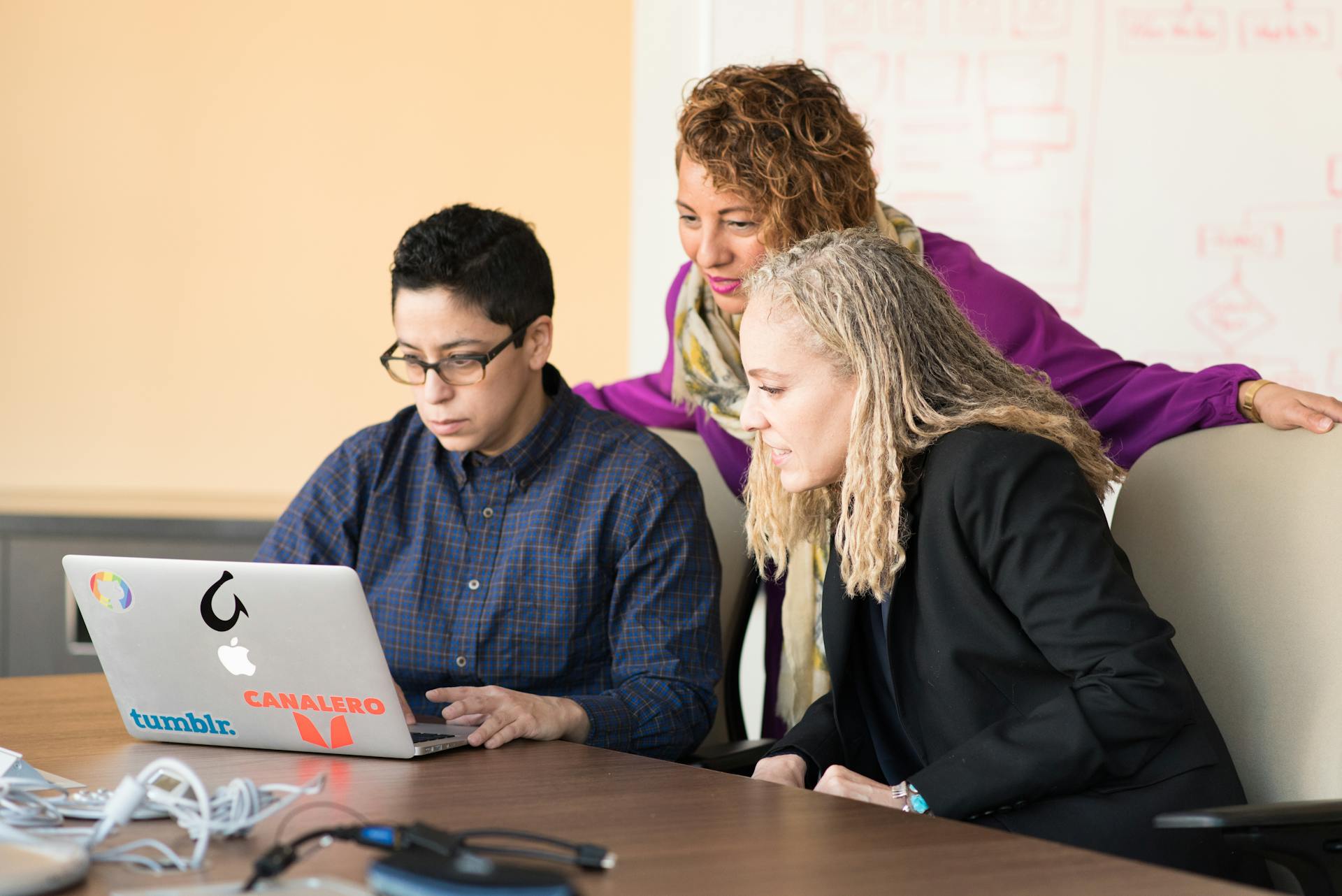 Team of three people collaborating on a laptop in an office setting.