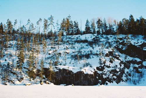 Free A scenic winter landscape featuring a snow-covered cliff with evergreen trees under a clear blue sky. Stock Photo