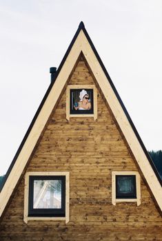 Woman enjoying a vacation in an A-frame cabin, sipping from a mug, and wearing a towel turban, gazing out the window.