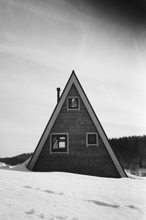 Grayscale Photo of a Wooden Cabin on a Snow-Covered Field