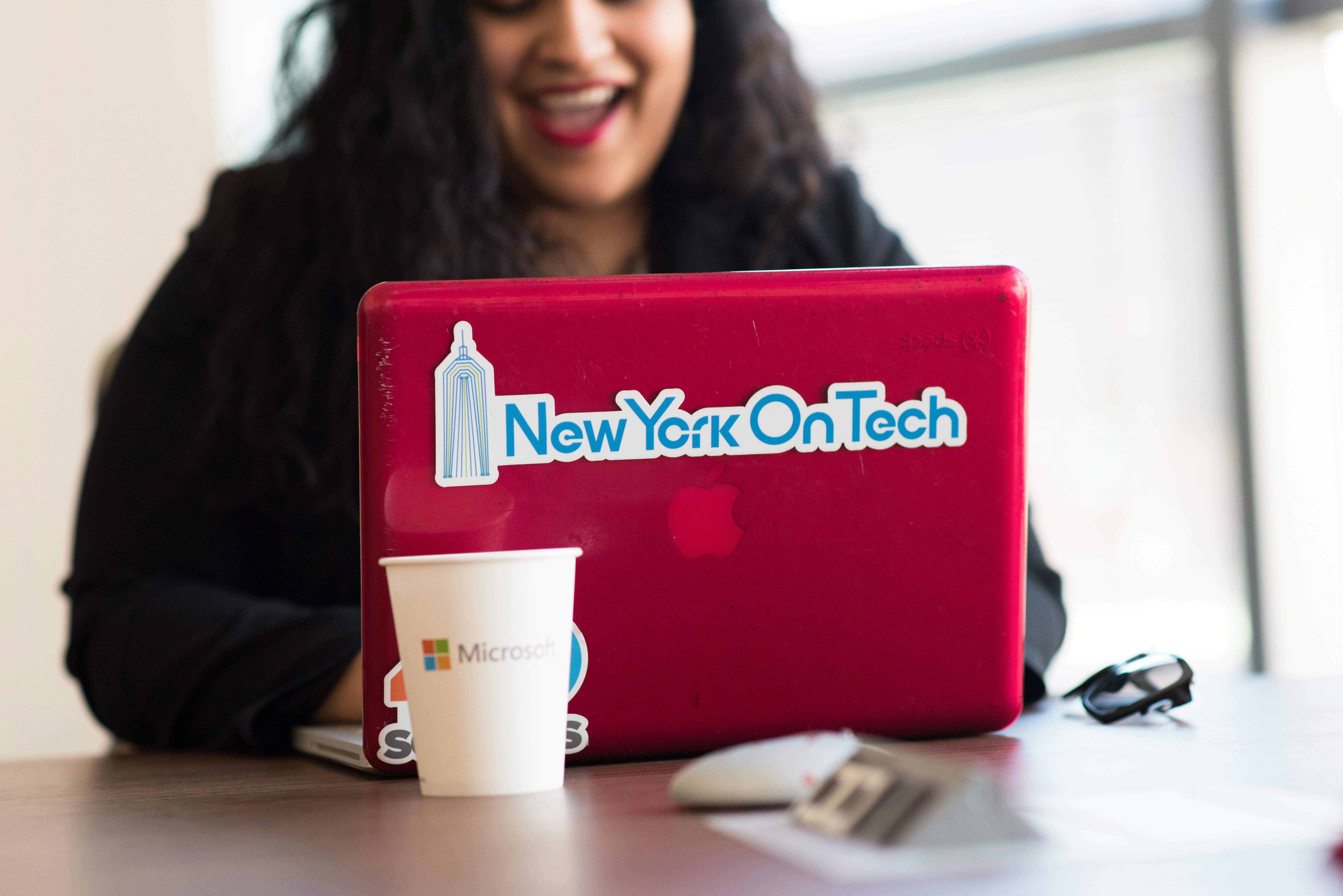 Young woman working remotely with a laptop in a modern indoor office setting, showcasing tech culture.