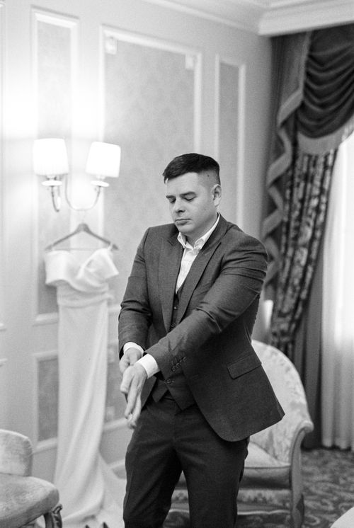 Free A groom in a suit adjusting his sleeves indoors, captured in black and white. Stock Photo
