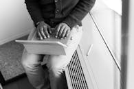 一张黑白照片里，一个人正坐在办公室的笔记本电脑前打字