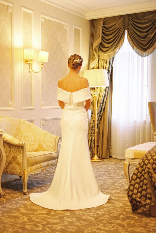 Free A graceful bride in a white wedding dress stands elegantly in a luxurious living room. Stock Photo