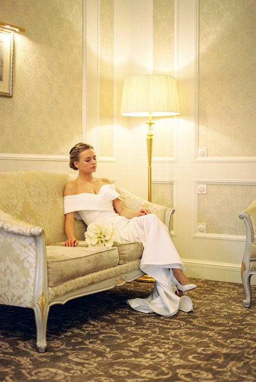 Free A bride in a white wedding dress sits elegantly on a vintage couch with a floral bouquet. Stock Photo
