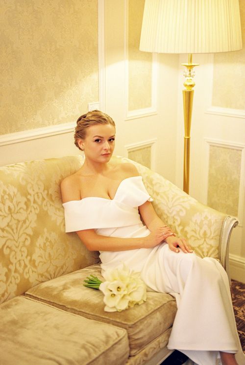 Free Elegant bride in a wedding dress sitting on a luxurious couch in a well-lit interior. Stock Photo