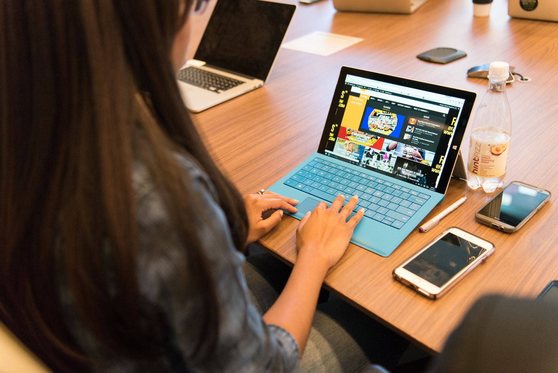 A woman working on a laptop at a wooden table with office devices around her.