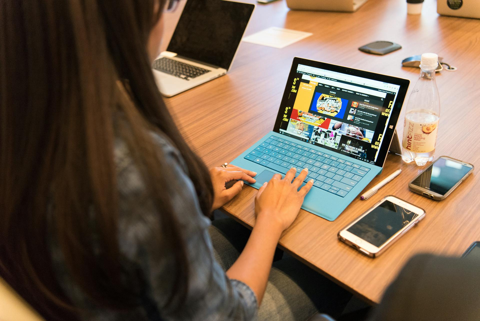 A woman working on a laptop at a wooden table with office devices around her.