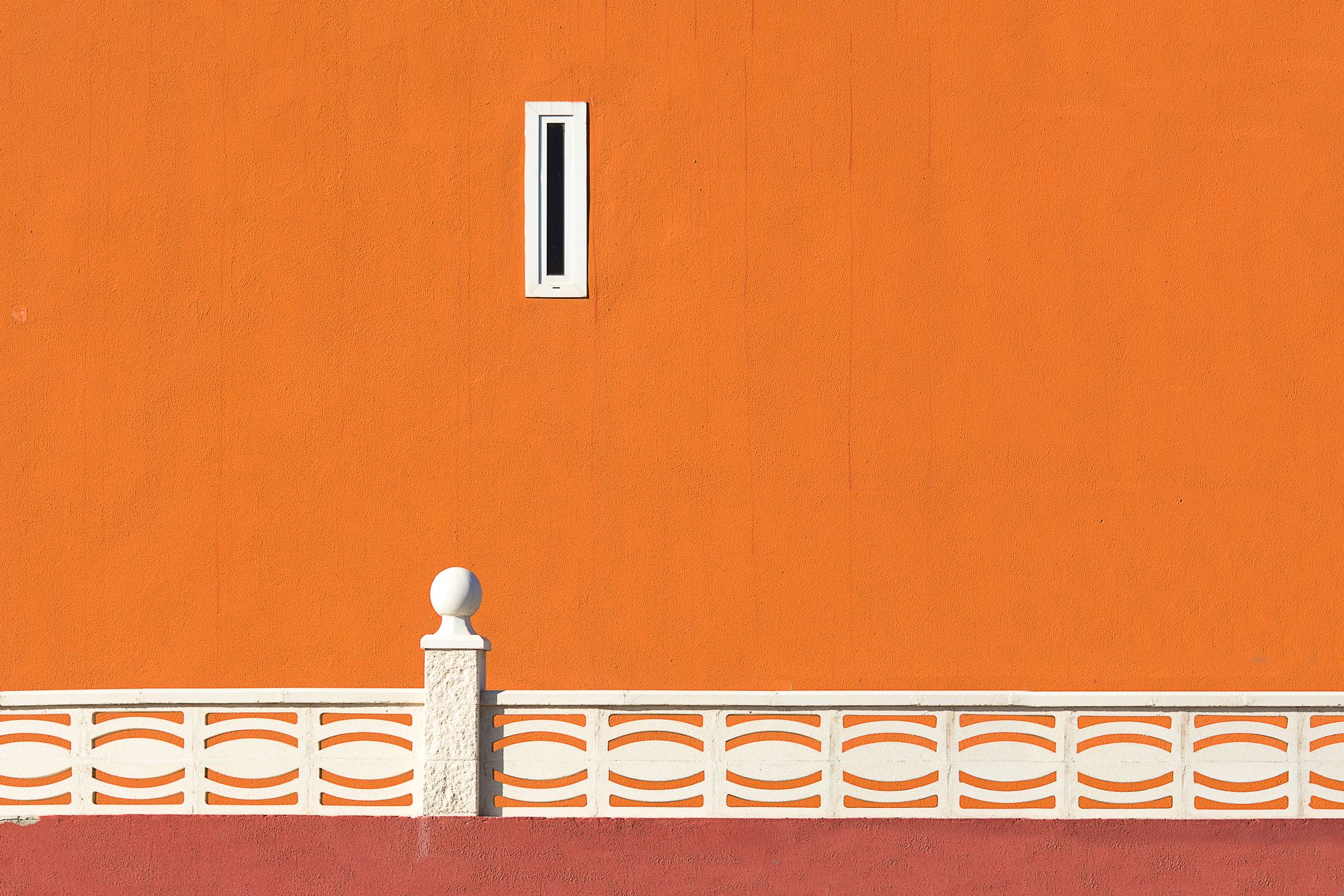 A bright orange wall with a white patterned railing