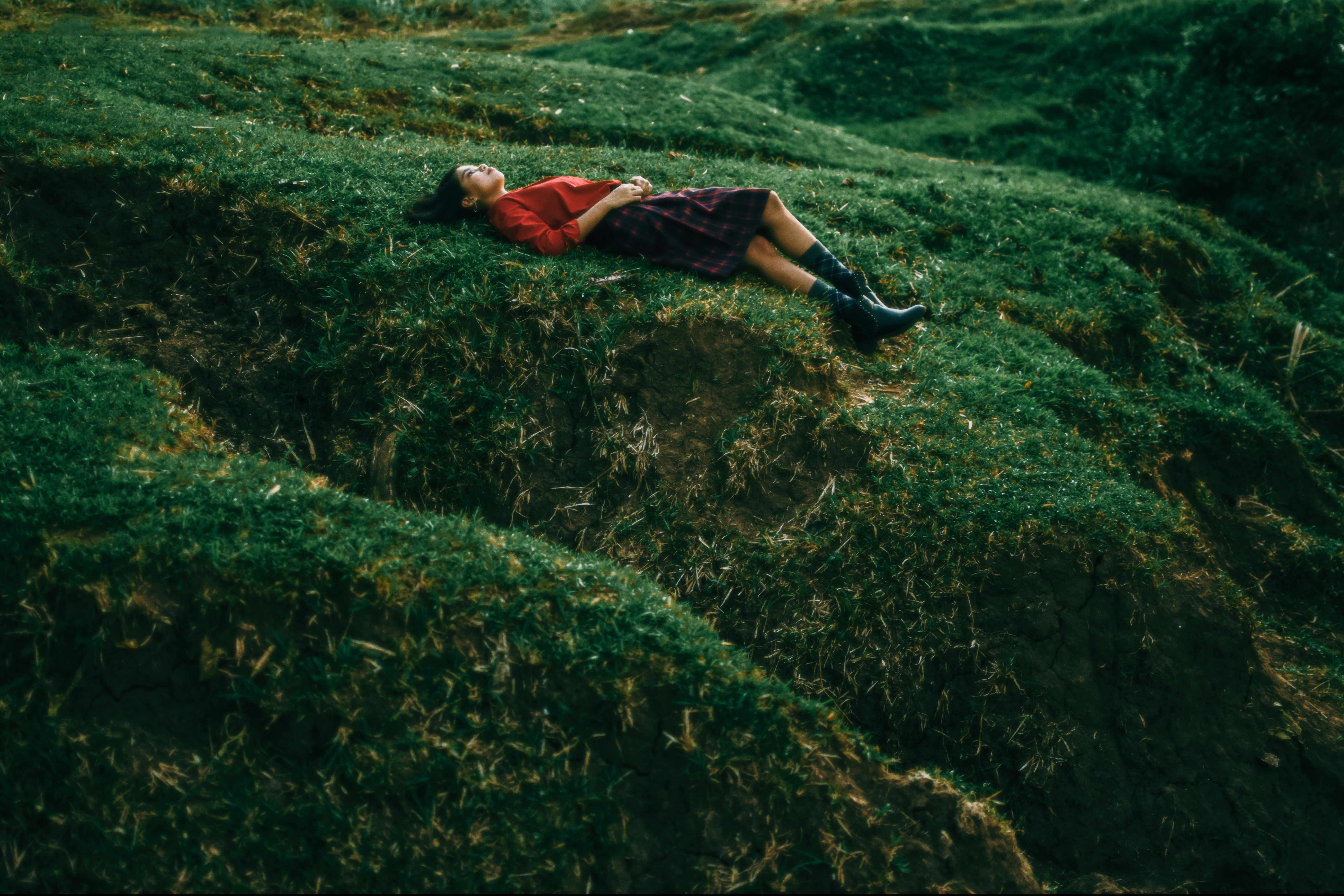 A serene woman in red relaxes on a lush green hillside, capturing tranquility and nature.