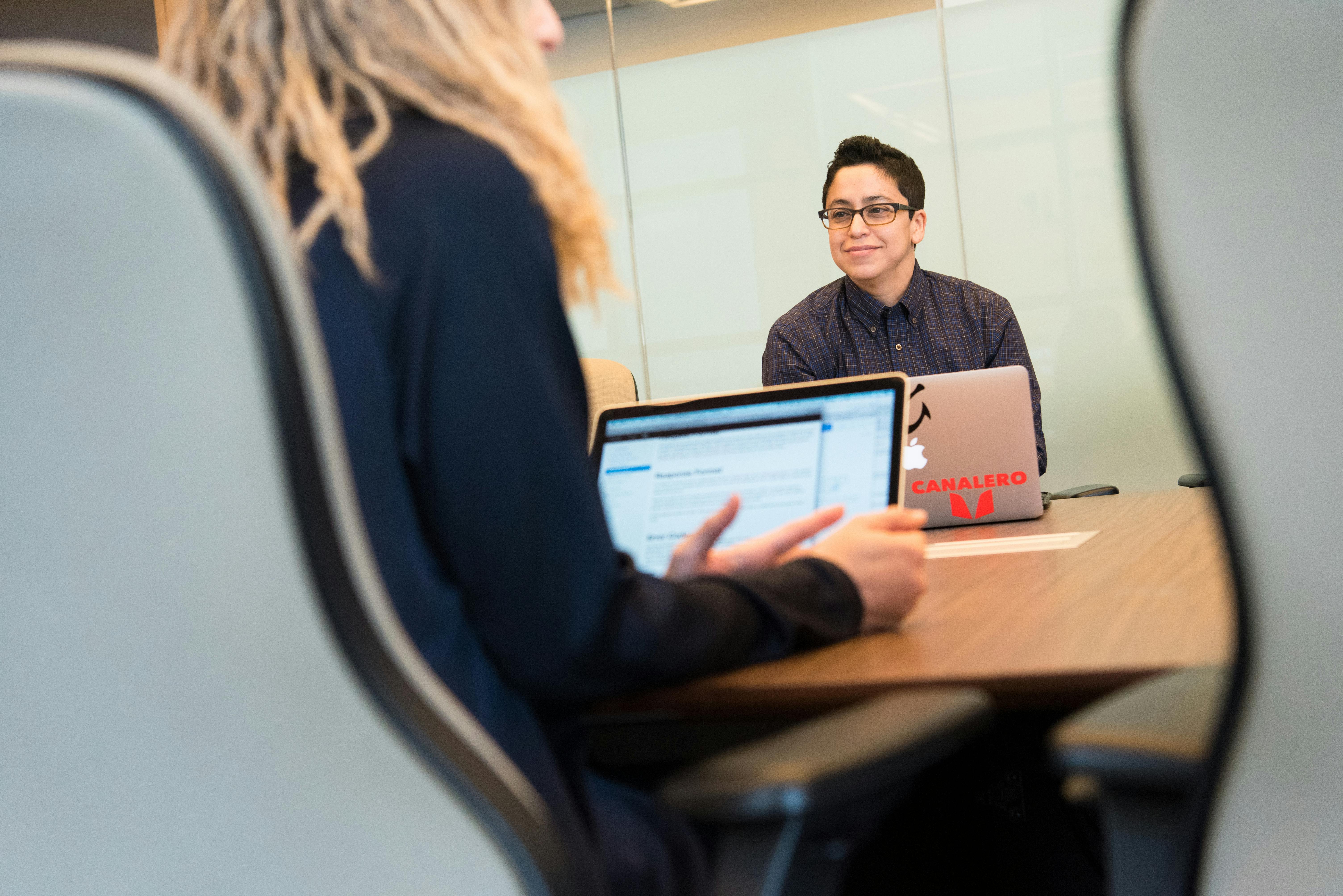 Two colleagues engaged in a business meeting with laptops in a modern office setting.