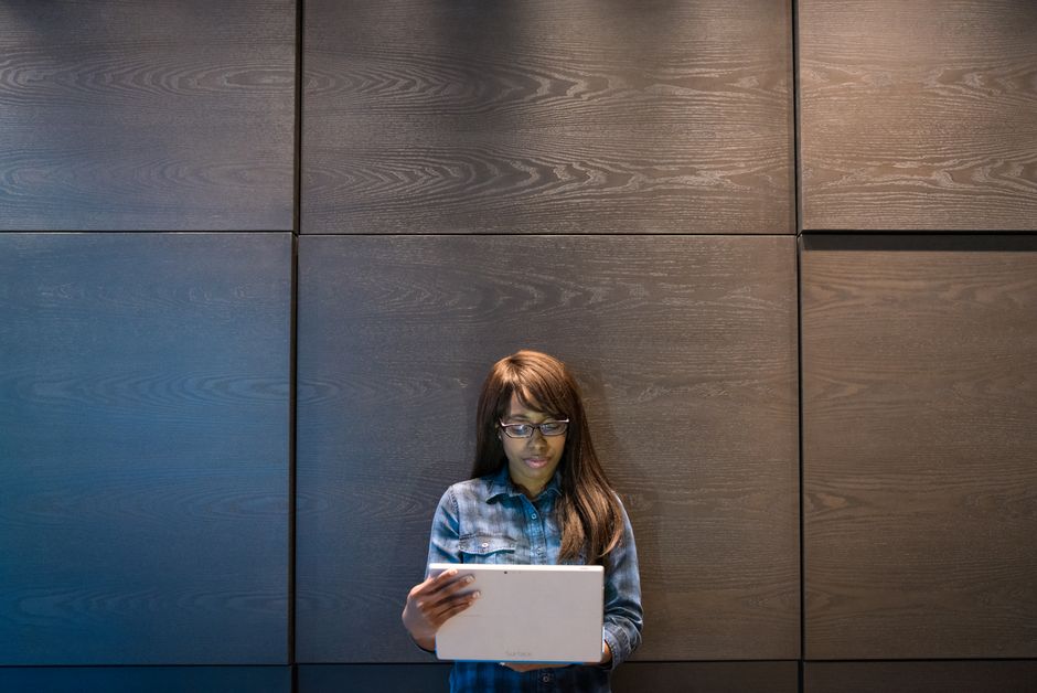Focused African American woman using a laptop against a wooden wall in a modern office setting.