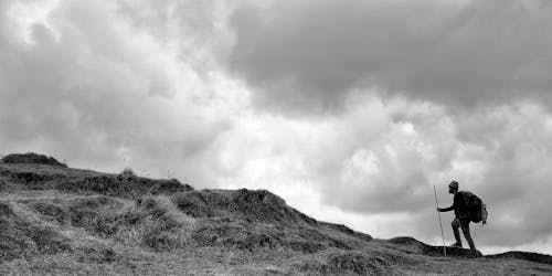 Grayscale Photo of Man Walking on the Mountain