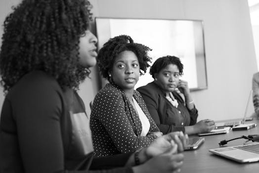 Three black women engaged in a serious discussion at an office meeting.