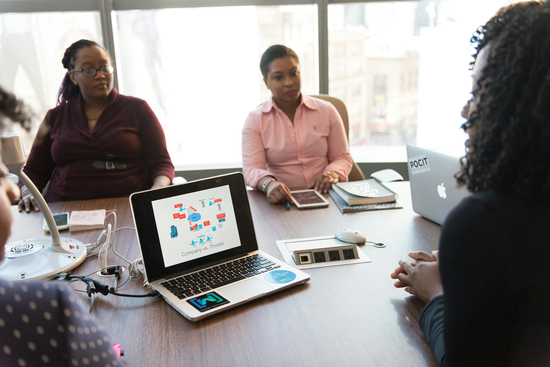 Business meeting with diverse team using laptops and tablets in a modern office setting.