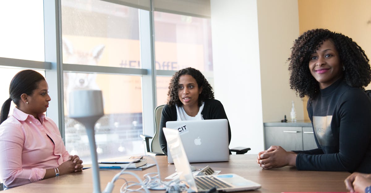 Three Woman Sitting Beside Brown Wooden Conference Table With Silver Apple Macbook