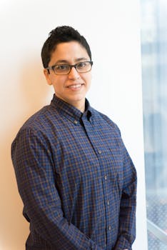 一个戴着眼镜、穿着休闲格子衬衫的人，在室内自信而友好地展示着肖像