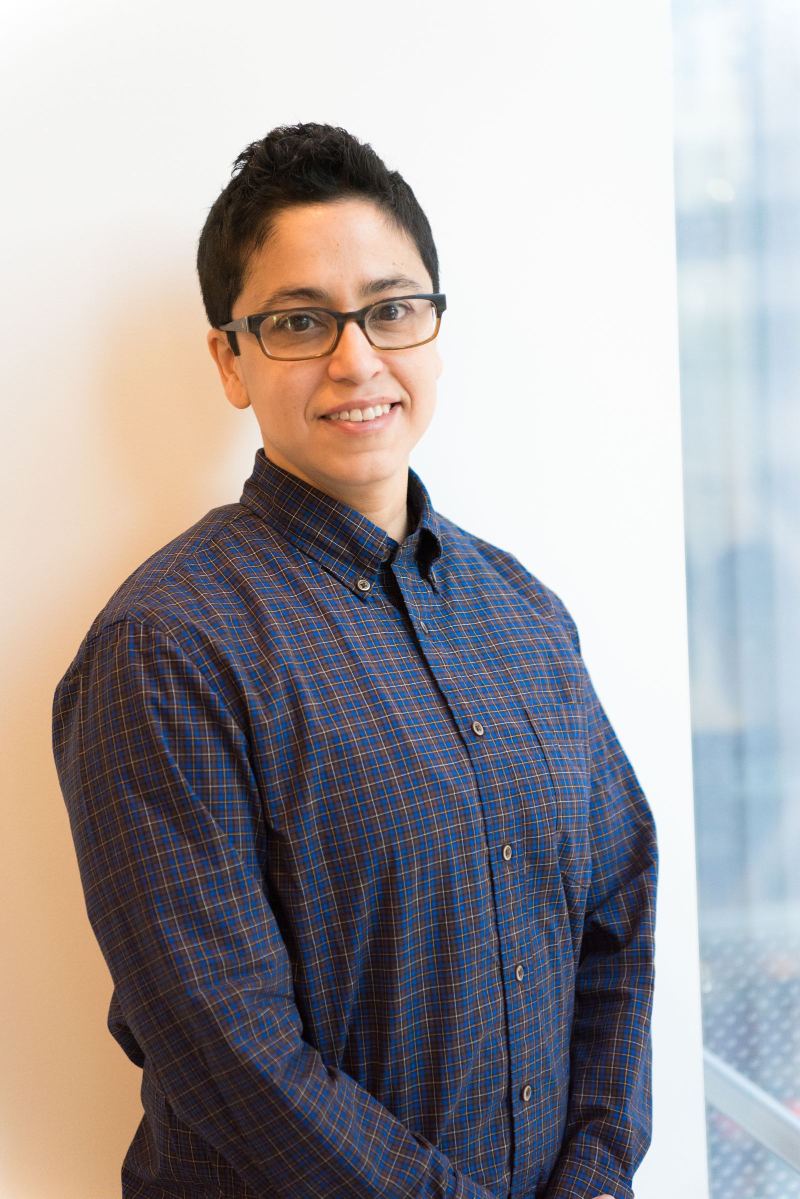 A person in glasses and a dark shirt standing by an office window