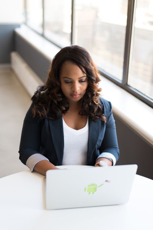 Free African American woman focused on laptop in a modern office setting with natural light. Stock Photo