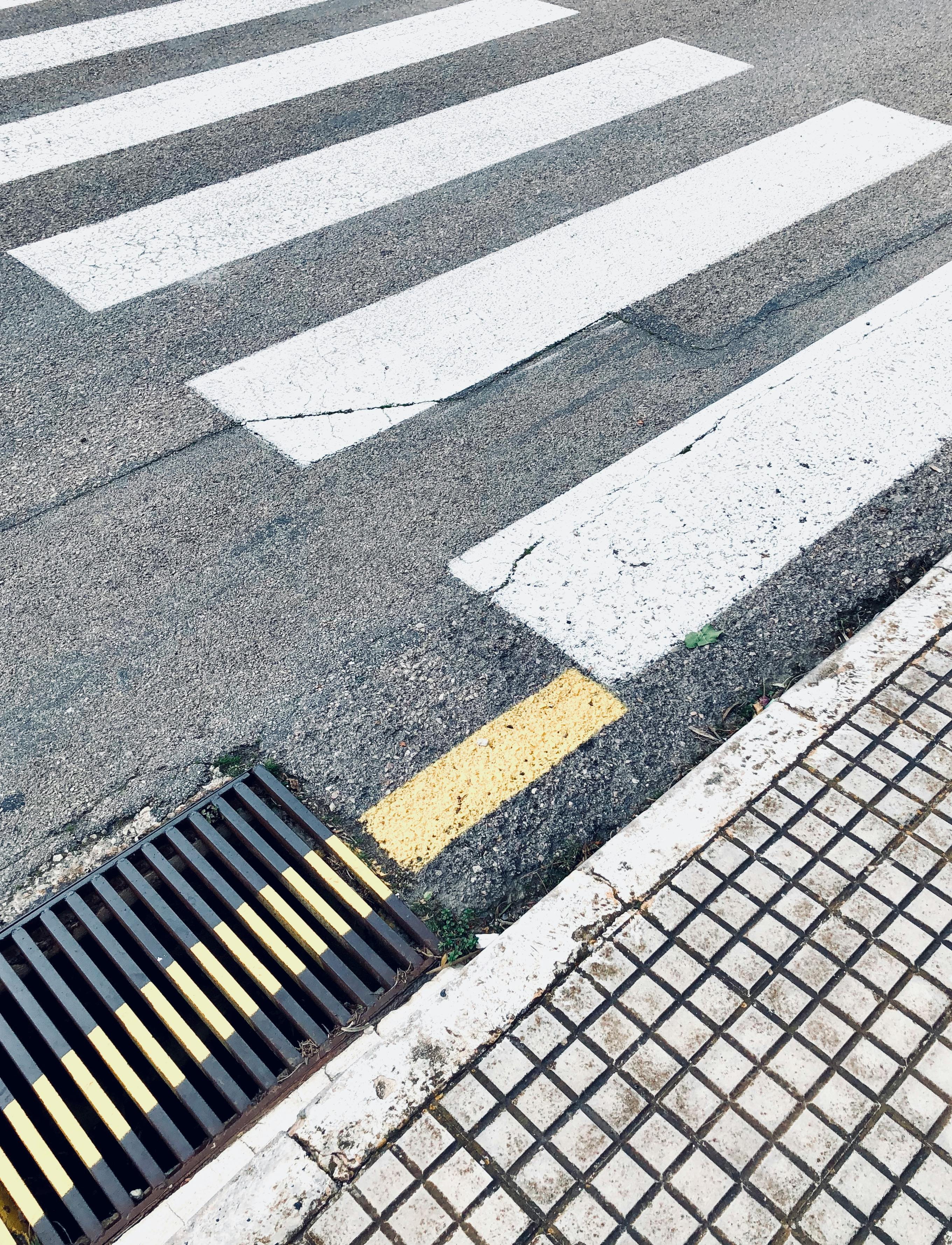 Crosswalk marked on asphalt road near sewer grid in city ...