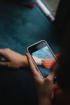 A hand takes a close-up photo of a wristwatch using a smartphone, displaying detail and fashion.