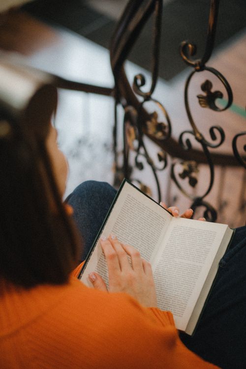 Free A woman reading a book while seated on a staircase, capturing a serene moment. Stock Photo