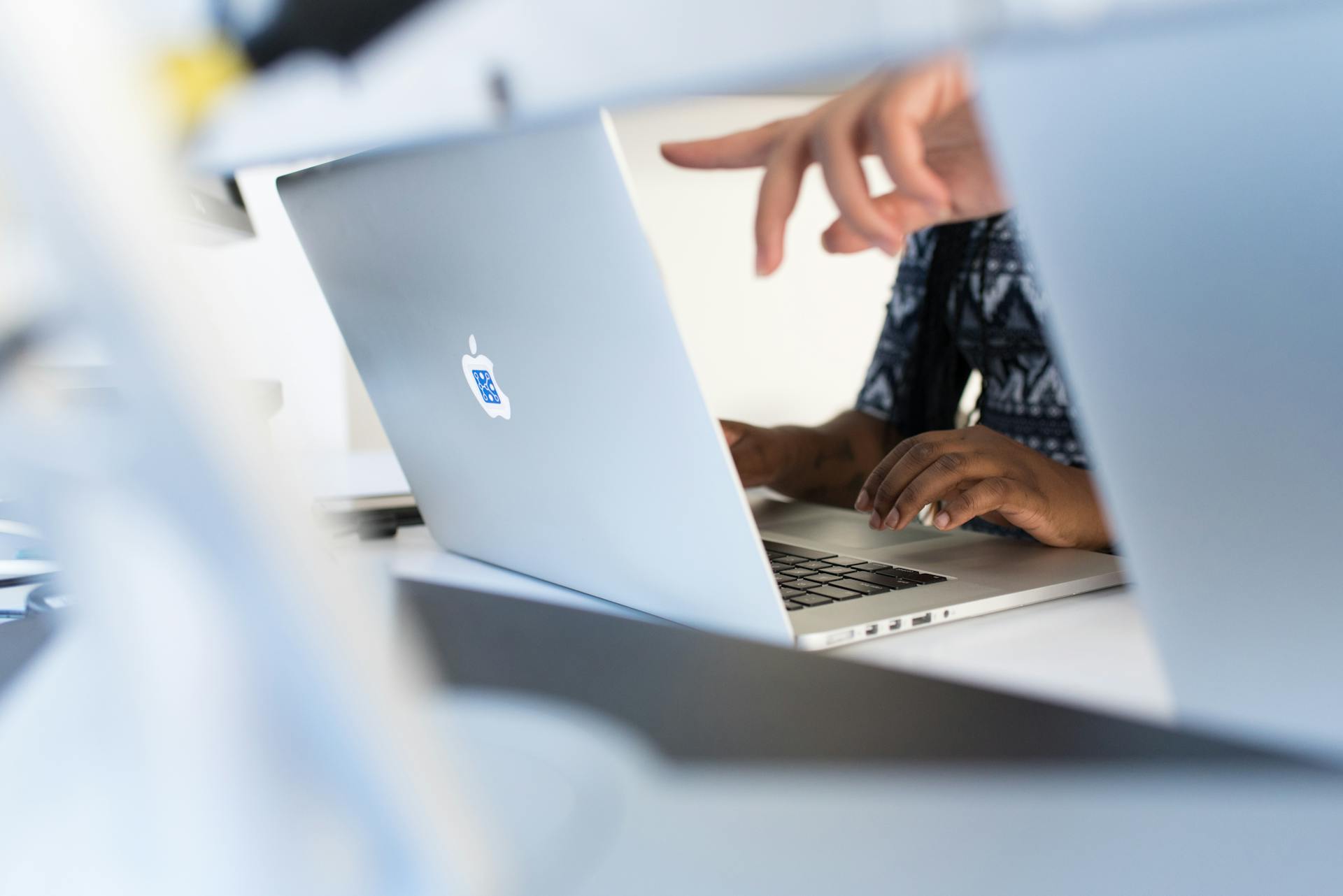 Hands working on a laptop in a modern tech office, showcasing teamwork and technology.