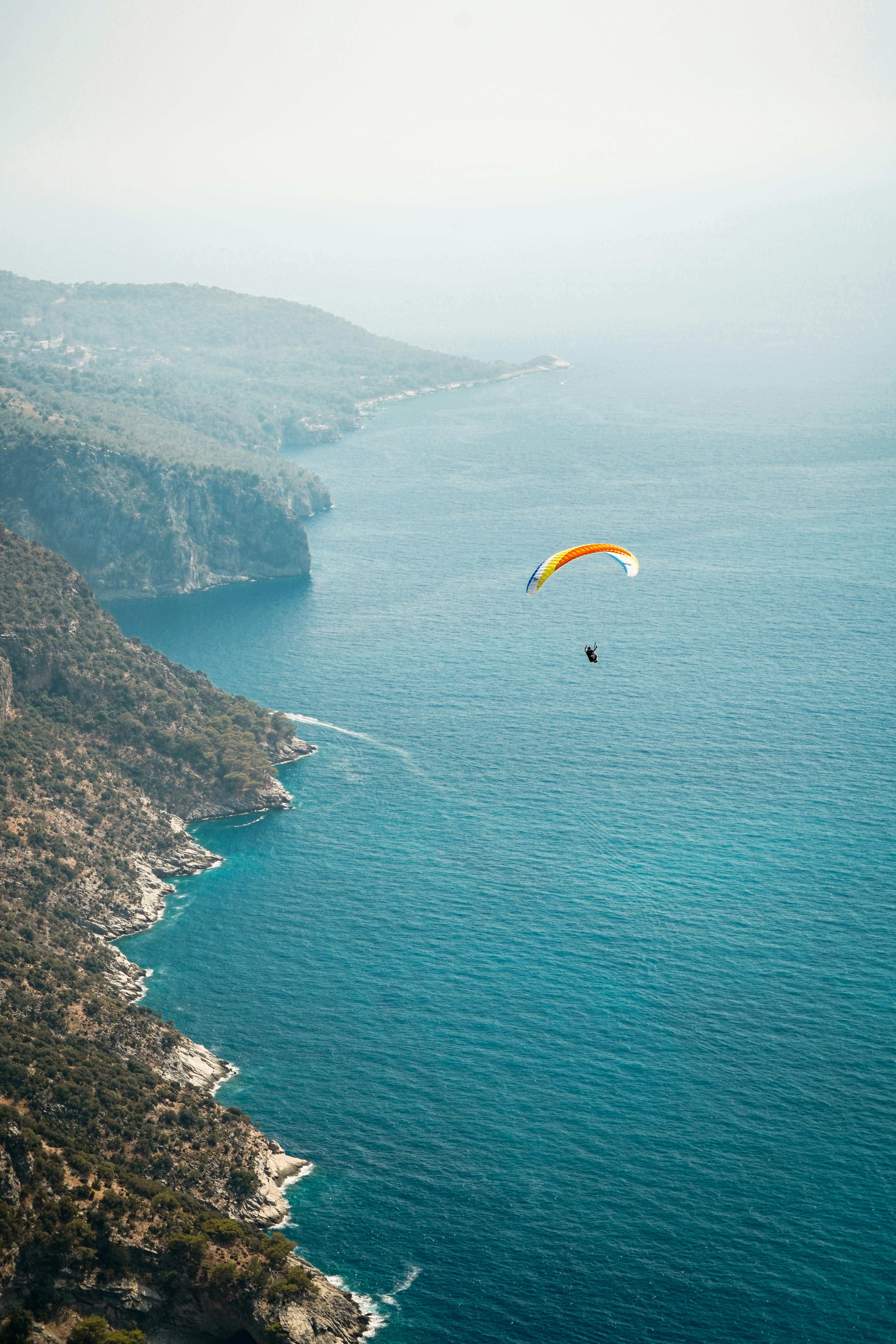 A breathtaking aerial view of a paraglider soaring over a stunning coastline and azure sea.