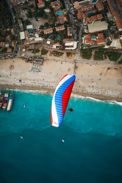 Free High-altitude view of a parachute gliding over a vibrant beach town and turquoise sea. Stock Photo