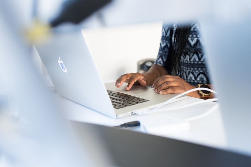 Woman typing on a laptop at a desk in a modern office setting, focused on work.